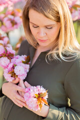 Freckled blonde pregnant woman in the park at spring with sakura trees, shallow depth of field pregnancy glow
