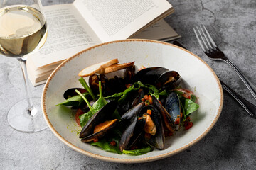 Mussels salad with fresh mini spinach on a grey stone table with a glass of white wine