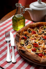 Close up of a lunch in an italian cafe: tomato and cheese pizza on a squared red tablecloth