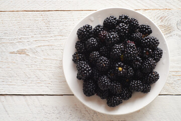 Fresh blackberries in a white plate on a white wooden background with space for text.