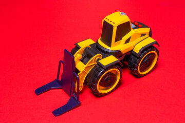 The yellow black forklift toy typewriter on a red background. Construction equipment tractor for children.