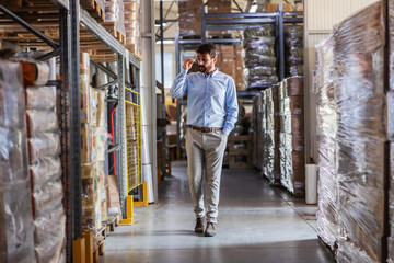 Full length of young attractive CEO walking trough warehouse and checking on goods.
