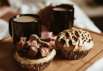 Blurred picture of dessert , sweet buns with cream on a wooden board. Out of focus cups of coffee. Breakfast in the bed.