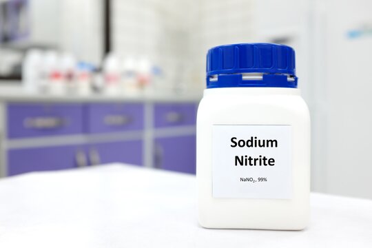 Selective focus of a bottle of sodium nitrite preservative chemical compound. White laboratory background with copy space.