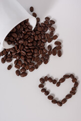 Coffee beans spill out of the cup on white background. Coffee heart