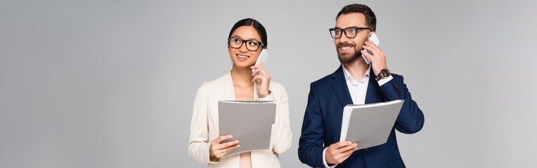 panoramic concept of interracial businesspeople talking on mobile phones while holding folders isolated on grey