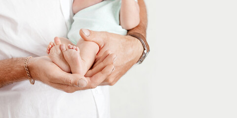 Baby feet in father hands. Tiny newborn baby's feet on male hands closeup. Dad and his child. Happy Family concept. Beautiful conceptual image of parenthood. Banner. Copy space