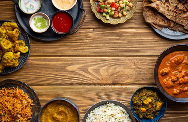 Assorted Indian home food, different dishes and snacks, wooden rustic table. Homemade Pilaf, butter chicken curry, palak paneer, chicken tikka, dal soup, naan bread, choice of chutney. Space for text.