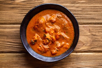 Indian chicken curry with tomato gravy on wooden rustic background. Traditional Indian dish butter chicken tikka masala, healthy lunch or dinner. Top view.