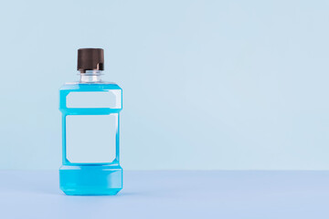 Mouthwash bottle with blank label for oral hygiene routine on light blue background. Mouth rinse liquids help to against bad breath, cavities and plaque. Dental care product. Copy space.
