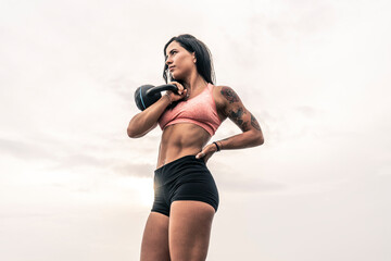Athletic woman exercising with kettle bell. Muscular woman working out outdoors.