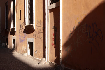 The evening light falls glancingly on one of the salmon-colored walls of a street in Rome.
