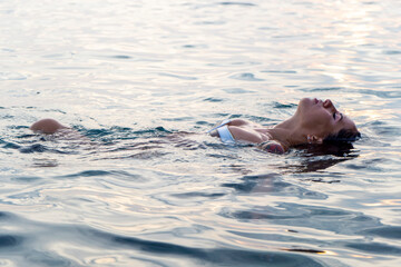 Obraz premium Beautiful young woman portrait floating in the sea at sunset, relaxing