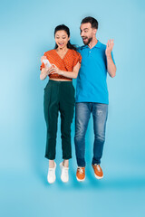 Fototapeta premium excited man touching asian woman using smartphone while levitating on blue