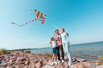Man hugging wife and daughter with kite on beach near sea