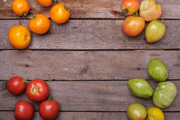 Green and red tomatoes are laid out in a circle on a wooden table, with free space in the center. Top view 
