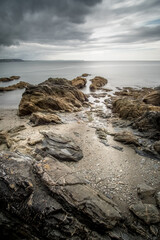 Cornish coast with moody sky, eroded rocks, and smooth water at low tide