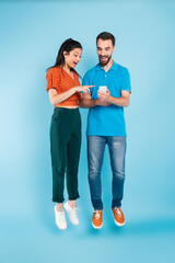 excited asian woman pointing with finger at smartphone in hands of bearded man while levitating on blue