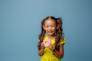 little Asian girl with long hair holds a doughnut in her hands and smiles at the Studio on a blue background