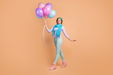 Full length photo of pretty lady carry many air balloons walking surprise party best friend wear lilac violet jumper green pants boots blue beret scarf isolated beige color background
