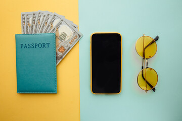 Travel planning with smartphone, sunglasses and passport with money on blue yellow background.