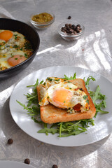 Tasty breakfast. Crispy Toast with fried egg and spices. Sandwich in a white plate with arugula. Light background. Vertical view