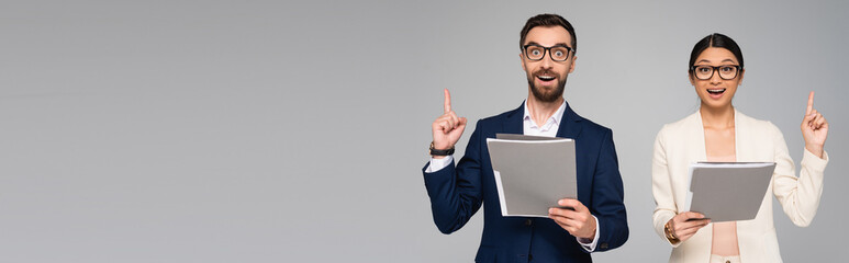 panoramic shot of excited couple of interracial businesspeople showing idea sign while holding...
