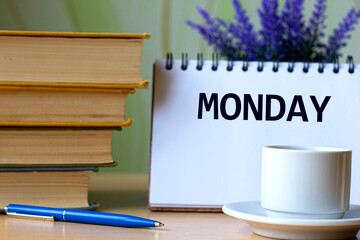 MONDAY - word in a notebook on a background of old books with pen and white cup