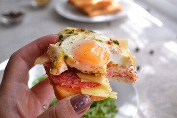 Tasty breakfast. Toast with egg, cheese and sausage. The girl holds a toast, a sandwich in her hand. Closeup.