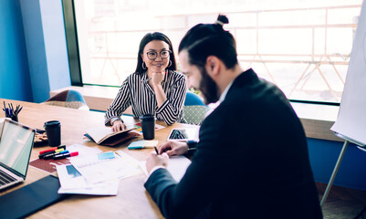 Smiling elegant ethnic adult businesswoman in workplace during meeting with coworker in office