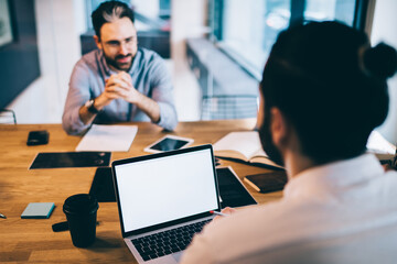 Men sitting at desk talking and using laptop at office