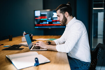 Fototapeta premium Serious manager using laptop and sitting at table in office