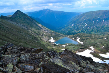 stones, view of mountain lake in form of heart among snow ice glaciers, green mountain ranges overgrown with trees, Chersky peak