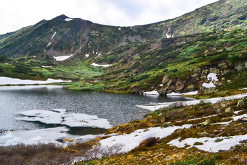 Fototapeta na wymiar mountain lake among snow glaciers in the summer green mountains overgrown with trees under cloudy sky, Siberia, Hamar-Daban