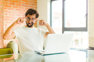 young bearded man with a laptop looking concentrated and thinking hard on an idea, imagining a...