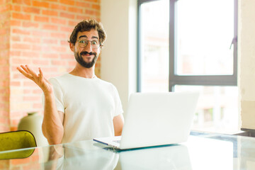 young bearded man with a laptop feeling happy, surprised and cheerful, smiling with positive attitude, realizing a solution or idea
