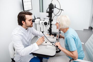 Concentrated optometrist checking eye for a patient using modern equipment. Eye exam and vision...
