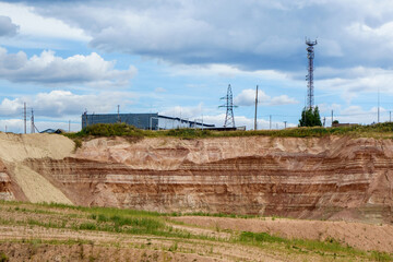 Panorama of working site in open pit mine. It can be seen underground layers of minerals. Upper part & background are containing high voltage towers & building for equipment & storage
