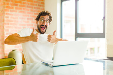 young bearded man with a laptop smiling broadly looking happy, positive, confident and successful,...