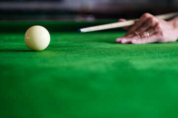 Man's hand and Cue arm playing snooker game or preparing aiming to shoot pool balls on a green billiard table. Colorful snooker balls on green frieze.