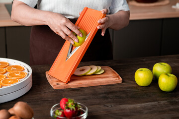 Close-up of unrecognizable woman using mandoline slicer for cutting apple while preparing fruits...