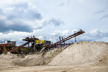 Stone crusher and its conveyor in industrial quarry. Dump of prosessed minerals are nearby