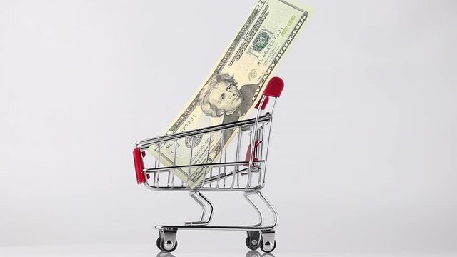 metallic shopping cart of red color with 20 dollar bill rotating against white and gray background, side view. wholesale and black friday sales concept
