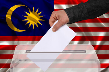 male voter drops a ballot in a transparent ballot box against the Malaysia national flag, concept of state elections, referendum