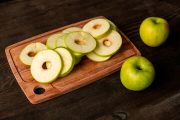 Close-up of green apple slices on cutting board and ripe apples on kitchen table, cooking concept