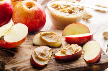 Cut board with apple slices with peanut butter on white wooden kitchen table