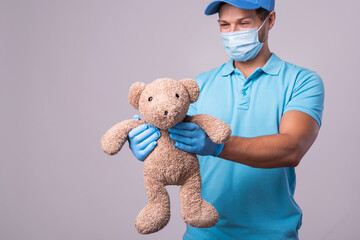 Young delivery man with a teddy bear is wearing prevention mask and gloves