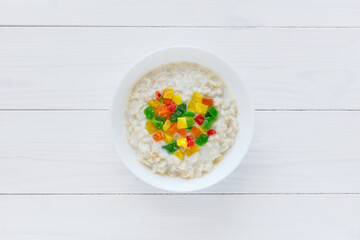 Oatmeal with candied fruits in a white plate on a white wooden background. Candied fruit in the shape of a heart. Top view of a healthy Breakfast. Creative composition. Copyspace