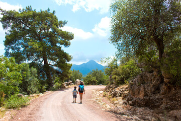 A woman with a backpack leads a child by the hand along a mountain trail.
