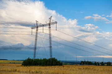 High voltage line tower is standing among farm field. Scenic sky is on background